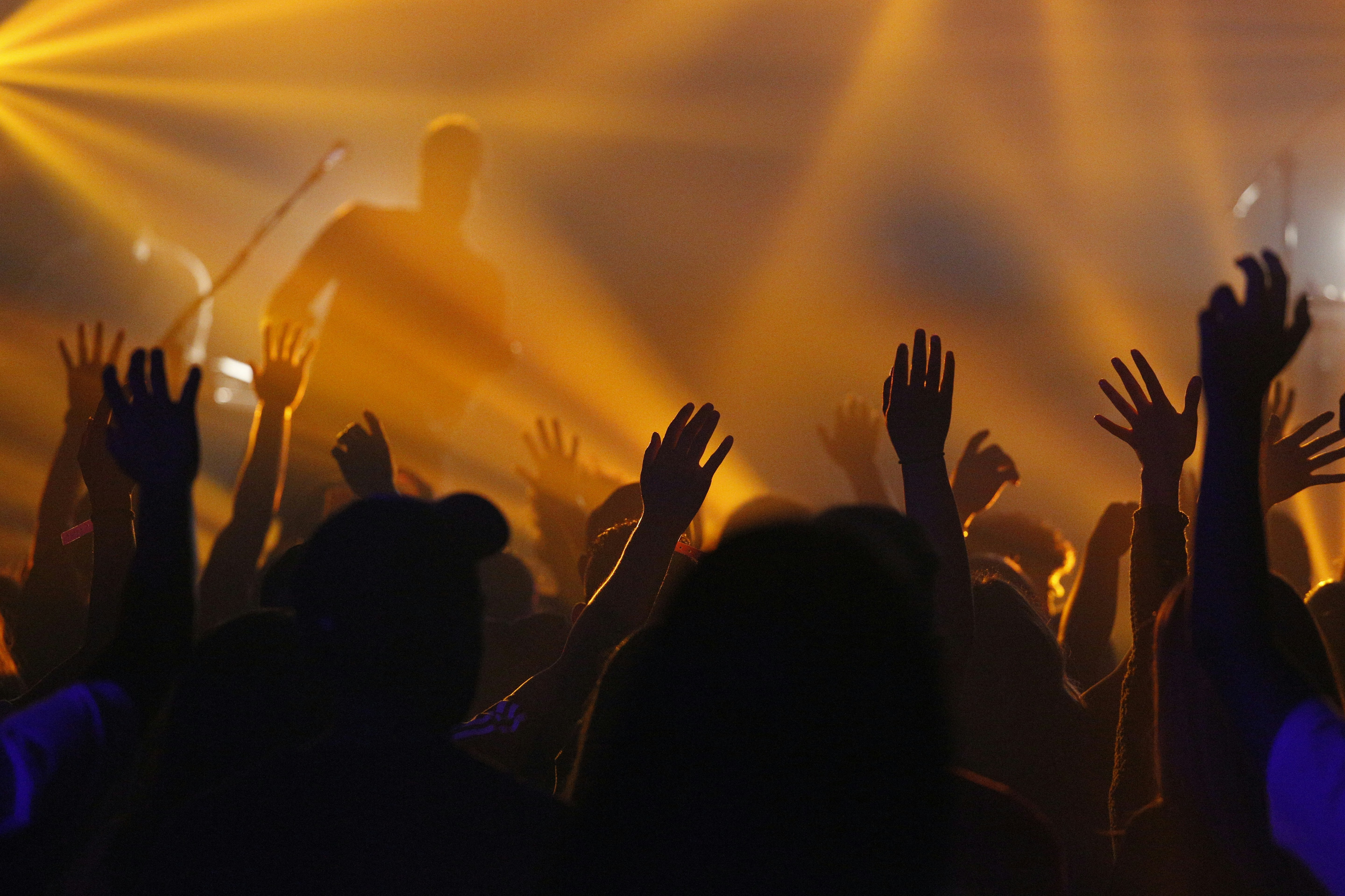 Concert crowd with hands raised under golden stage lights